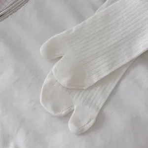 Close-up detail of white split-toe ribbed mid-tube socks, soft fabric texture display.