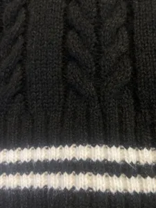 Close-up detail of black cable knit sweater fabric with white horizontal stripes