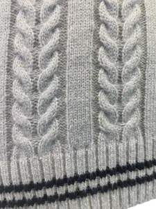 Detailed macro view of the cable knit pattern and striped ribbed hem on grey vest