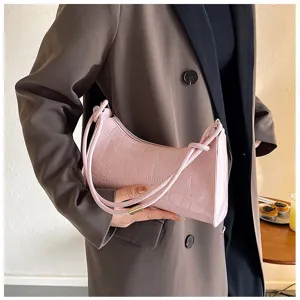 Detail of a pink crocodile pattern underarm bag held by a model in a brown blazer.