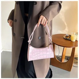 Lifestyle detail of a pink croc-patterned bag held by a model in a cafe setting