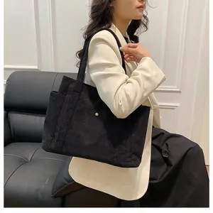 Grande borsa tote in velluto a coste nera indossata da una modella in un set moderno.