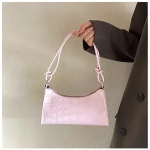 Handheld view of a pink faux-croc underarm bag with decorative strap knots