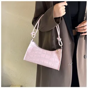 Chic pink crocodile pattern underarm bag held by a model in a stylish coat