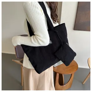 Detalle de bolso tote de pana negra con bolsa pequeña llevado por una modelo en sala