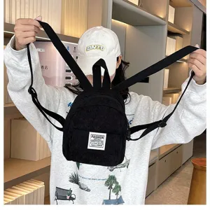Close-up of a black corduroy mini backpack held by a model in a casual indoor setting