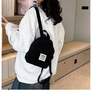Stylish black corduroy mini backpack for women shown being worn in a casual indoor setting