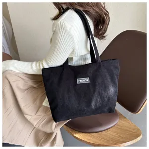 Detalle del bolso tote de pana negra con parche 'FASHION' sobre un conjunto informal