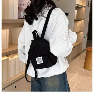 Stylish black corduroy mini backpack shown on a model in a cozy bookstore setting