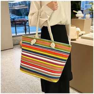 Kleurrijke gestreepte canvas draagtas met touwhandvatten gedragen door een model.