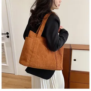 Grande borsa tote in velluto a coste arancione indossata da una donna in un interno.