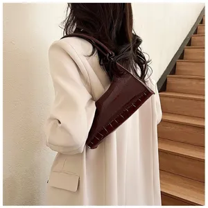 Detail of a brown crocodile embossed underarm bag worn with a chic beige blazer.