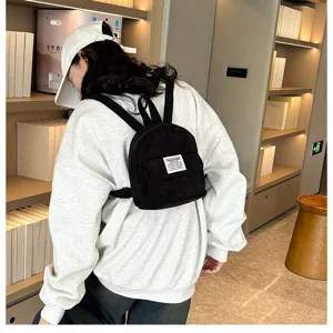 Detailed back view of a stylish black corduroy mini backpack worn by a model in a library