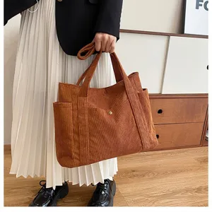 Primo piano di una borsa tote in velluto a coste marrone tenuta da una persona con un outfit.
