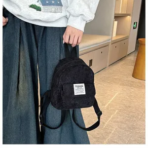 Detail view of a black corduroy mini backpack held by a model in casual streetwear