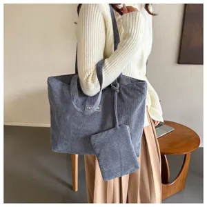 Bolso tote grande de pana gris con bolsa pequeña a juego llevado por mujer con cárdigan blanco