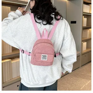 Rear view of a model wearing a pink corduroy mini backpack in a library setting