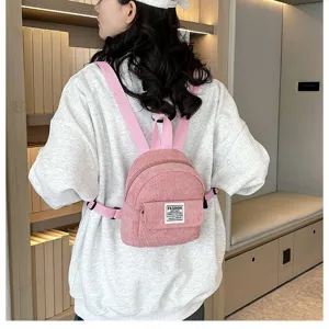Detailed view of a pink corduroy mini backpack worn by a model in a casual indoor setting.