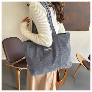 Bolso tote grande de pana gris para mujer llevado al hombro en un ambiente moderno