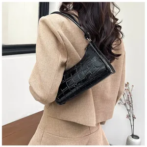 Detail of a chic black crocodile embossed underarm bag worn with a tan blazer jacket