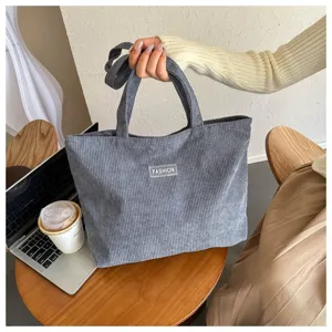 Primer plano de un bolso tote de pana gris con parche FASHION en un entorno de estilo
