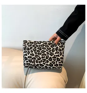 Nahaufnahme einer Hand, die die Textur der Clutch aus Canvas mit Leopardenmuster zeigt