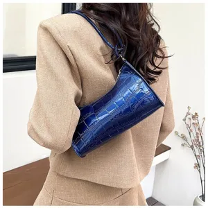 Glossy blue croc-embossed underarm bag on model's shoulder, elegant fashion accessory.