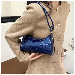 Detailed view of a navy blue crocodile-embossed underarm bag held by a model.