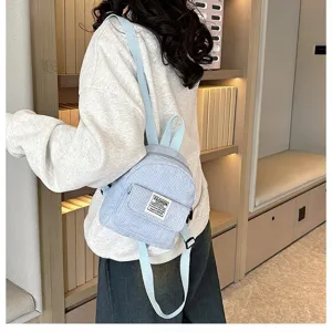 Close-up detail of a light blue corduroy mini backpack worn by a model in a cozy library