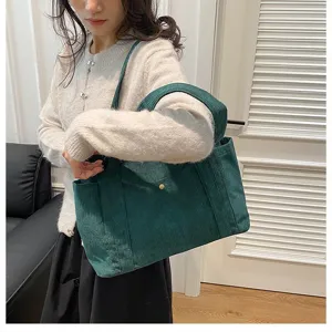 Vista dettagliata della borsa tote in velluto a coste verde scuro indossata da modella