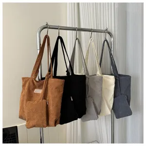 Vista detallada de bolsos tote de pana multicolores colgados en un soporte metal