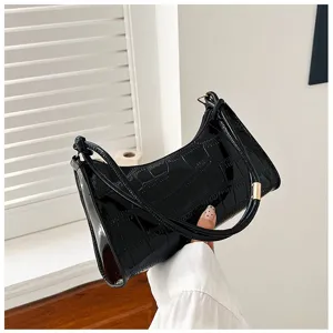 Elegant black faux crocodile baguette bag with a shiny finish being shown in a hand.