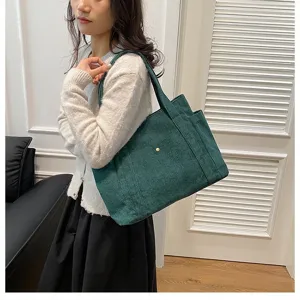 Borsa tote in velluto a coste verde scuro mostrata come dettaglio sulla spalla del modello