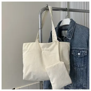 Primer plano de un bolso tote de pana crema con bolsa a juego en un perchero metálico.