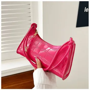 Detailed view of a stylish bright pink croc-embossed underarm bag held by hand