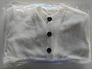 Detail view of a white knitted cardigan sweater inside protective clear plastic packaging