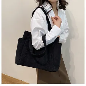 Dettaglio di una borsa tote in velluto a coste nera con grande capacità e tasche laterali.