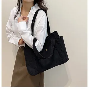 Dettaglio di un'elegante borsa tote in velluto a coste nero portata a spalla per un look casual