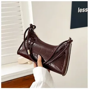 Detail view of a shiny dark burgundy crocodile-embossed underarm baguette bag for women