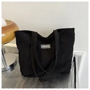 Primer plano de bolso tote de pana negro con etiqueta FASHION en mesa metálica.