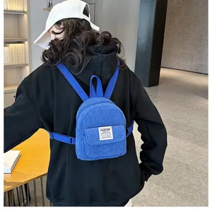 Detailed back view of a woman wearing a stylish blue corduroy mini backpack in a cafe.