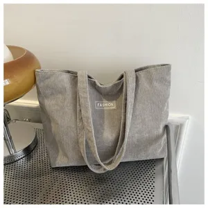 Primer plano de un bolso tote de pana gris con parche 'FASHION' para uso casual.