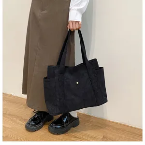 Primo piano di una grande borsa tote in velluto a coste nera tenuta da una modella