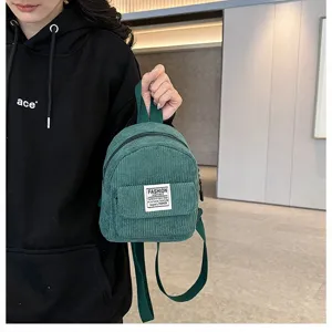 Green corduroy mini backpack shown held by a model for a casual outdoorsy look