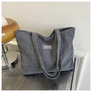 Vista detallada de un bolso tote de pana gris con etiqueta 'Fashion' y textura de canalé