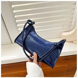 Detailed view of glossy dark blue stone pattern underarm baguette bag held against a white wall