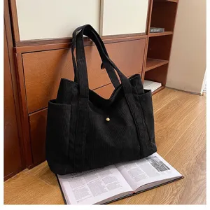 Grande borsa tote in velluto a coste nera appoggiata su una rivista in un ambiente casa.
