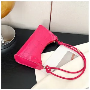 Close-up of hot pink crocodile textured underarm bag with unique knotted rope straps.