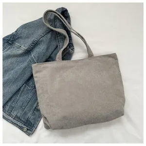 Bolso tote de pana gris para mujer sobre fondo blanco con una chaqueta vaquera decorativa