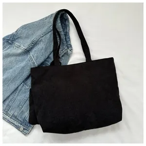 Vista detallada de un bolso tote de pana negra con un diseño informal y sencillo.